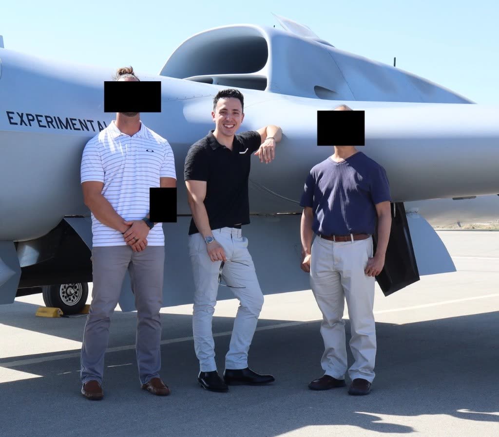 Daniel Heinen, center, standing on a tarmac in front of an experimental aircraft. Two people beside him have their faces redacted.