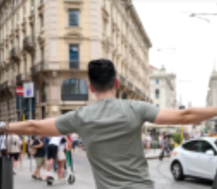 The retrieved photograph: a man seen from behind with his arms outstretched in a city street, buildings and tram wires behind him.