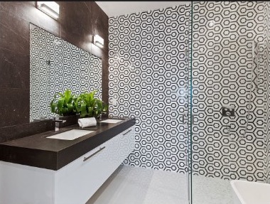 Property photograph of the matched bathroom, showing the same hexagonal tile, frameless glass shower enclosure, and dark stone surfaces