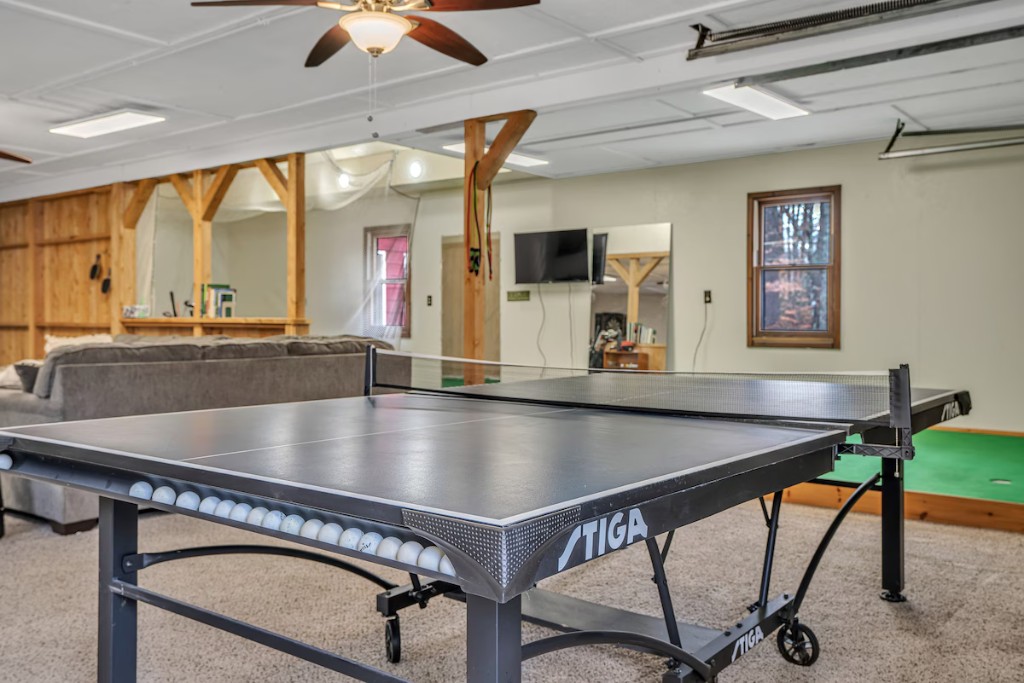 The matching listing photograph: the same room with a ping-pong table in front, showing the same timber posts and knee braces, window, wall-mounted TV and putting green