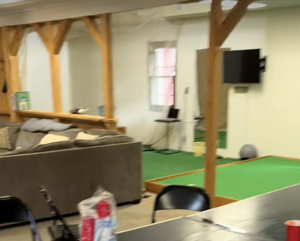 The source image: a frame from a video inside a games room, with timber posts and knee braces, a putting green, a small window and a wall-mounted TV